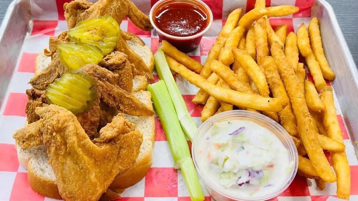 Fried chicken wings on white bread with pickles, celery, fries, coleslaw and red sauce